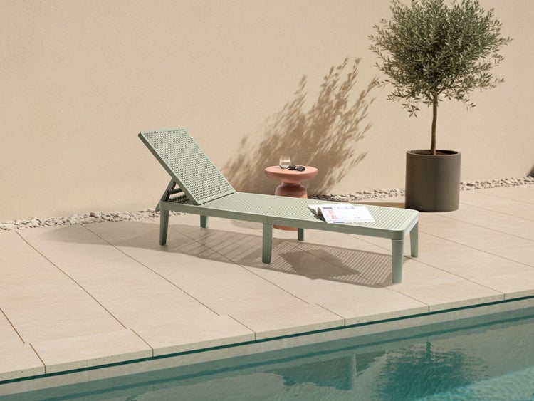 Liege aus Kunststoff neben Pool, Tisch und Pflanze
