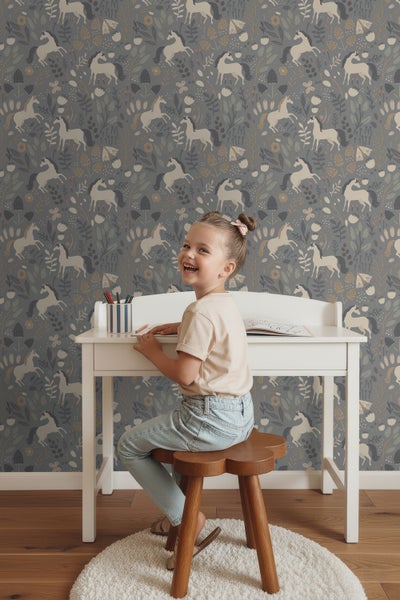 Mädchen sitzt an einem Schreibtisch vor einer Wand mit Einhornmuster.