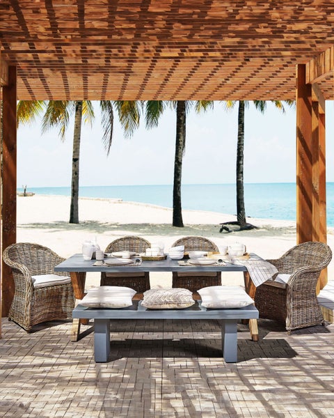 Gedeckter Esstisch mit Rattansesseln und Holzboden unter einer Holzpergola am Strand