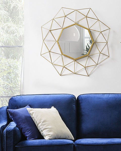 Dekorativer Wandspiegel mit geometrischem Design über einem blauen Sofa