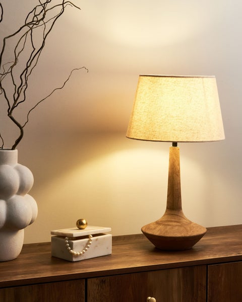 Dekorative Szene mit einer eingeschalteten Tischleuchte, einer Vase mit Zweigen und einer Schmuckschatulle auf einem Holzschrank.