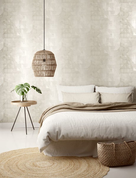 Schlafzimmer mit geometrischer Tapete, geflochtener Hängelampe, Bett, rundem Teppich und Beistelltisch