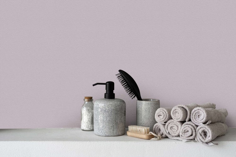 Strukturierte Tapete in Mauve in einer Badezimmerszene mit Seifenspender, Haarbürste und Handtüchern auf einer Ablage.