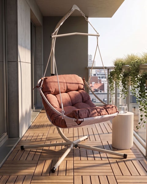 Moderner Hängesessel mit Metallgestell und dickem Polster auf einem Balkon mit Holzfliesen, Beistelltisch und Pflanzen.