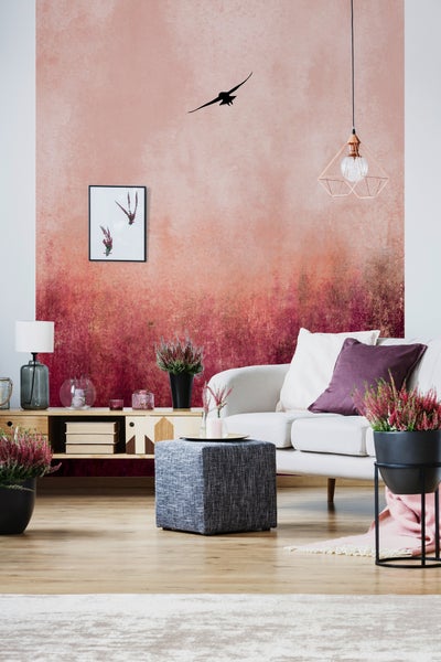 Wohnzimmer mit Verlaufstapete in Rosa und Burgunderrot. Ein weißes Sofa, grauer Hocker und ein Holzsideboard werden durch Heidekraut ergänzt.