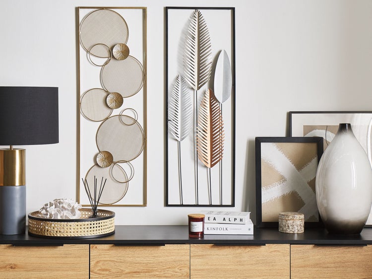 Wohnzimmerdekoration mit zwei Wandbildern, Tischlampe und dekorativen Accessoires auf einer Holzkommode.