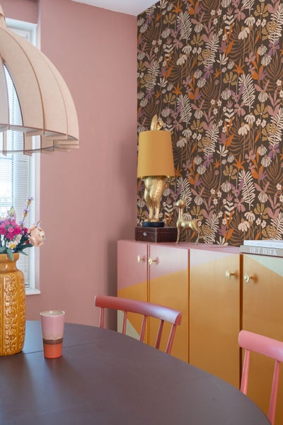 Esszimmer mit Esstisch, Stühlen, Sideboard, Lampe und floraler Tapete.