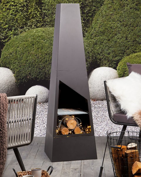 Moderner pyramidenförmiger Gartenkamin aus schwarzem Metall auf einer Terrasse mit gemütlichen Sitzgelegenheiten und Brennholz.