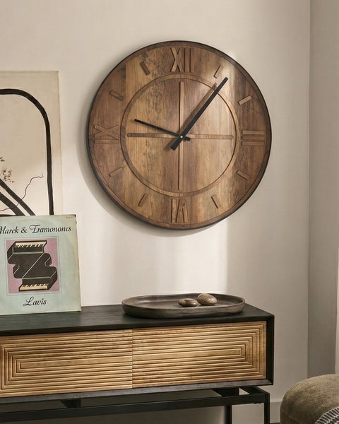 Große runde Wanduhr aus Holz mit römischen Ziffern, hängend über einer Anrichte in einem modern eingerichteten Raum.