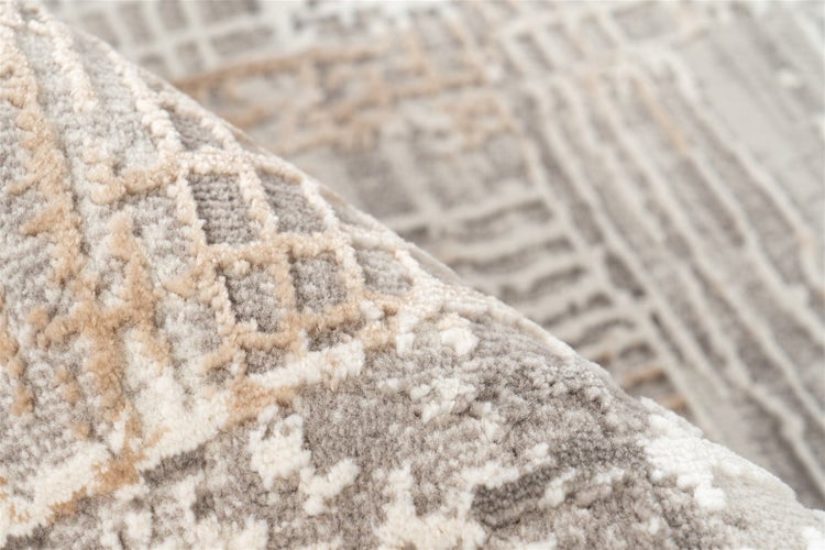 Detailansicht eines Teppichs mit abstrakten geometrischen Mustern in Grau, Beige und Weiß, weiche Oberflächenstruktur.