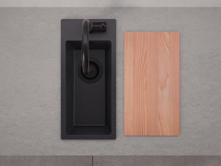Draufsicht auf eine kleine schwarze Verbundspüle mit schwarzer Armatur und einem Holzschneidebrett auf einer grauen Arbeitsplatte.