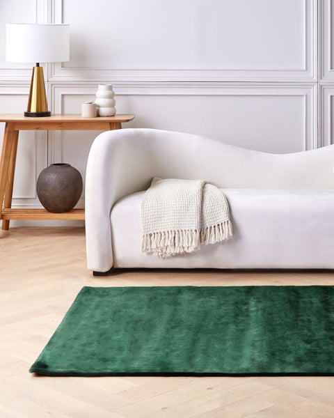 Wohnzimmer mit Sofa, Tischlampe und grünem Teppich