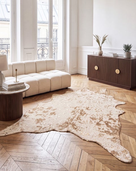 Wohnzimmer mit hellem Sofa, brauner Kommode mit Rillen, Beistelltisch und gemustertem Teppich auf einem Fischgrätparkettboden in einem Altbau.