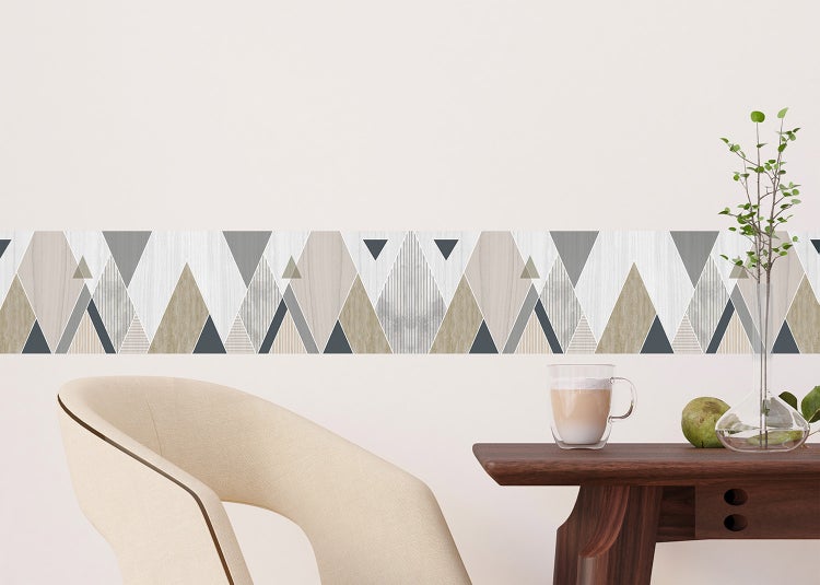 Tapetenbordüre mit geometrischem Dreiecksmuster auf heller Wand in modernem Zimmer mit hellem Sessel und dunklem Holztisch.