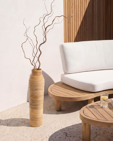 Moderne Outdoor-Lounge mit geschwungenem Holzsofa, weißen Polstern, Holztisch und hoher, geriffelter Korbvase mit dekorativen Zweigen.