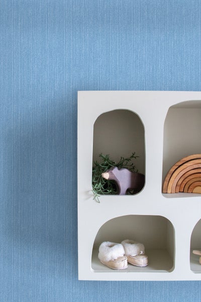 Regal mit Holzspielzeug und Babyschuhen vor einer strukturierten Wand