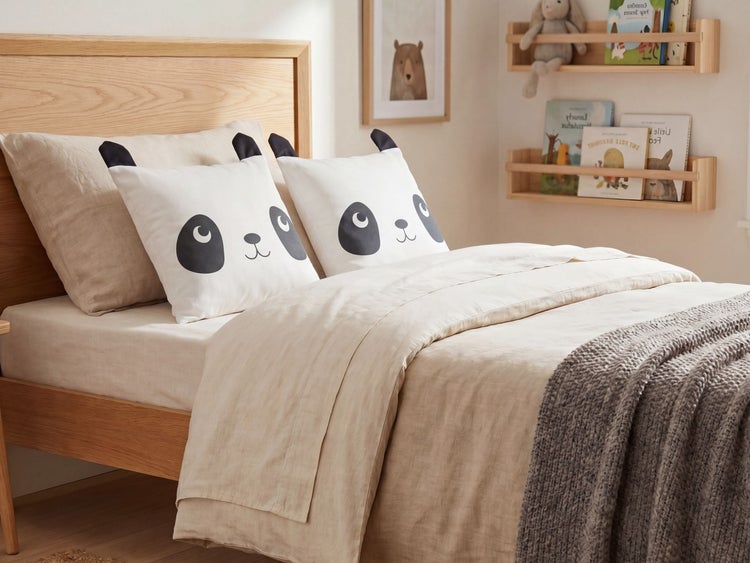 Kinderbett aus Holz mit Leinenbettwäsche, zwei Panda-Dekokissen und einer grauen Strickdecke in einem hellen, organisierten Zimmer.