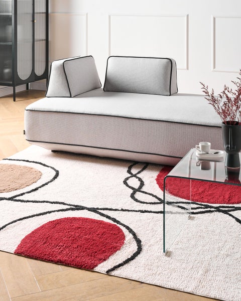 Modernes Wohnzimmer mit hellgrauem Sofa, gemustertem Hochflor-Teppich mit roten und schwarzen Kreisen und einem gläsernen Beistelltisch.