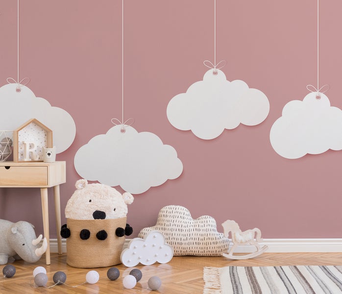 Kinderzimmer mit dekorativen Wolken an der Wand, Holzmöbeln, Stofftieren, einer Wolkenlampe und einem gemusterten Teppich.