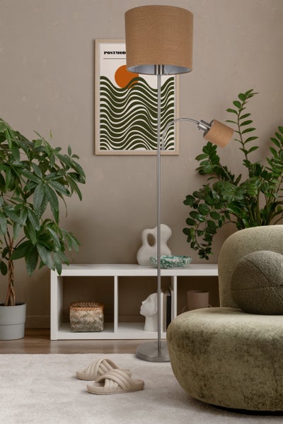 Wohnzimmer mit Stehlampe, Poster und Zimmerpflanzen auf einem weißen Teppich.