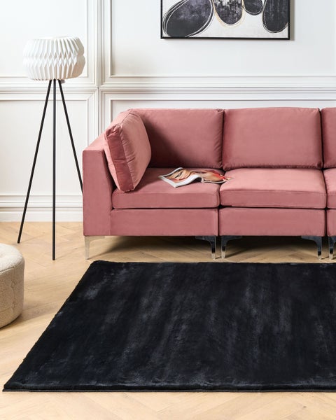 Wohnzimmer mit rosa Sofa, Stehlampe und schwarzem Teppich