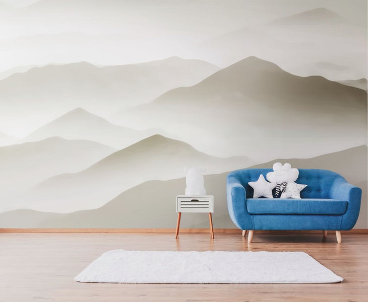 Dekoratives Zimmer mit Bergtapete, blauem Sofa, weißem Teppich und Beistelltisch