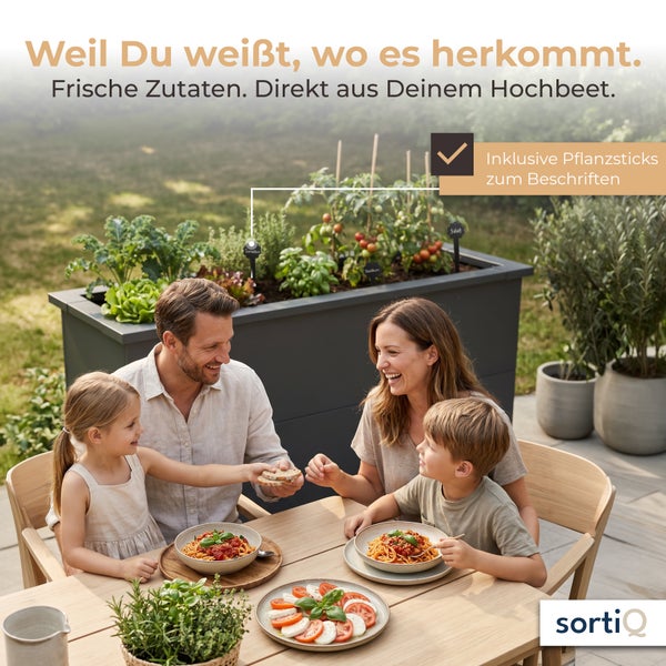 Familie isst im Freien an einem Holztisch neben einem dunkelgrauen Metall-Hochbeet mit Pflanzen und Pflanzsticks zum Beschriften. sortiQ Logo.