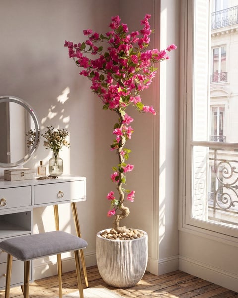 Künstliche Bougainvillea mit pinken Blüten im weißen Topf in einem hellen, organisierten Zimmer neben einem Schminktisch.