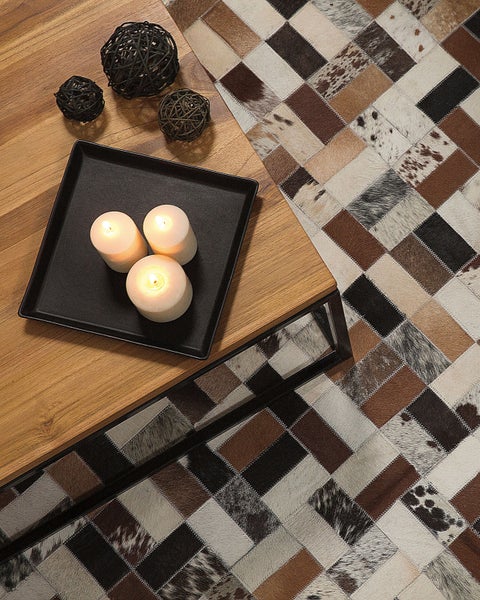 Patchwork-Teppich in Felloptik unter einem Couchtisch aus Holz mit schwarzem Metallgestell, dekoriert mit brennenden Kerzen und Rattankugeln.