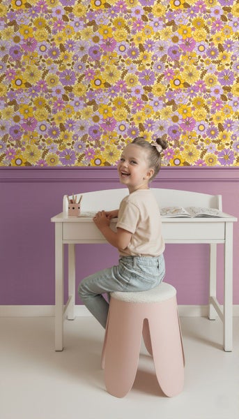 Kind sitzt an einem Schreibtisch vor einer Wand mit Blumenmustertapete