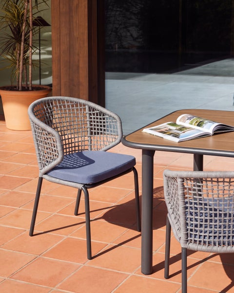 Gartenstuhl mit geflochtener Rückenlehne und Sitzkissen am Terrassentisch auf einer gefliesten Terrasse