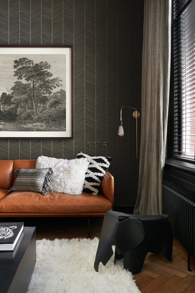 Wohnzimmer mit braunem Ledersofa, gemusterter Tapete und dekorativen Kissen