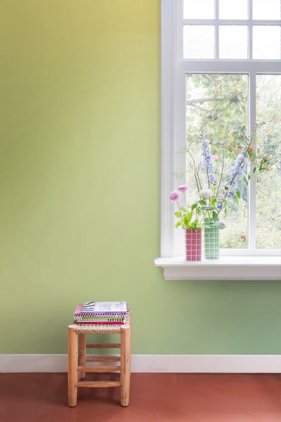 Helles Zimmer mit einem Fenster, auf dem zwei Vasen mit Blumen stehen, und einem kleinen Hocker mit Notizbüchern