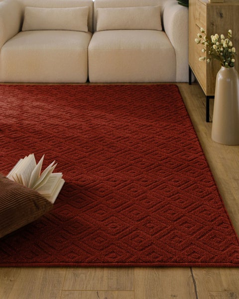 Roter Teppich mit geometrischem Rautenmuster in einem hellen, ordentlichen Wohnzimmer auf Holzboden.