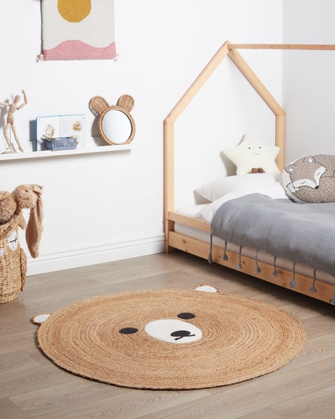 Hell eingerichtetes Kinderzimmer mit rundem Juteteppich im Bärengesicht-Design, Hausbett aus Holz, Wandregal und geflochtenem Korb.