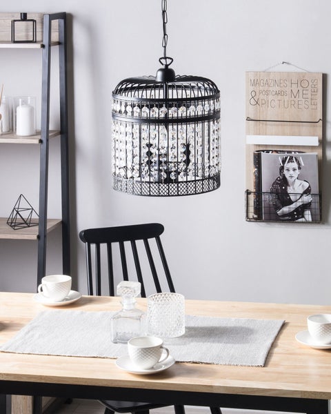 Innenaufnahme eines Esszimmers mit einem Holztisch, einem Regal und einer schwarzen Käfig-Hängeleuchte mit Kristallen.