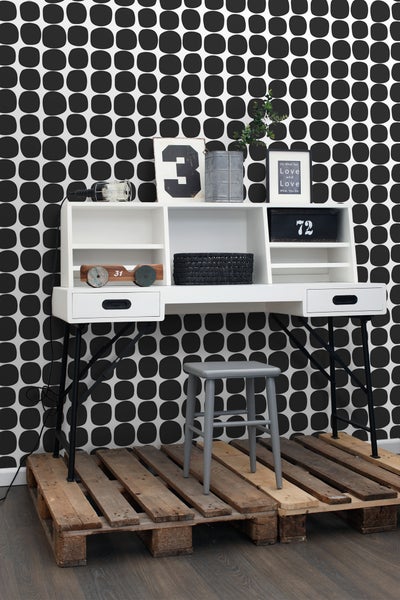 Arbeitszimmer mit Schreibtisch, Hocker und dekorativen Gegenständen vor einer gemusterten Tapete