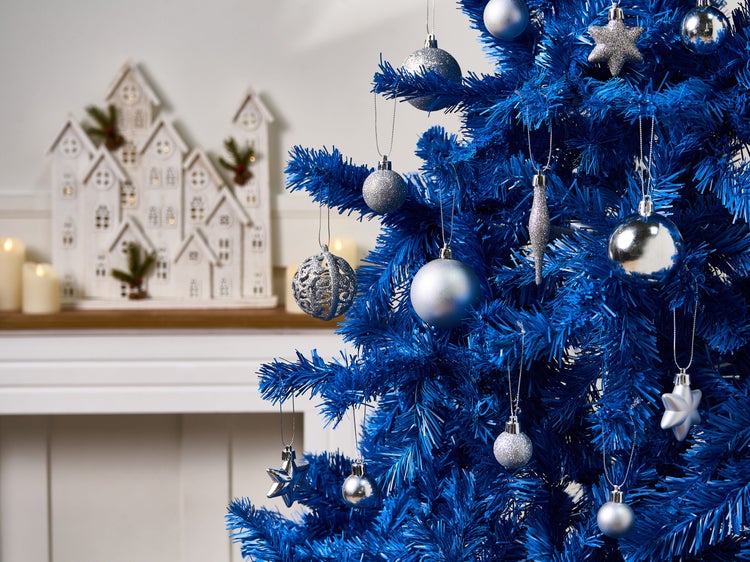 Dekorierter blauer Weihnachtsbaum mit silbernen Weihnachtskugeln und Dekohäusern im Hintergrund