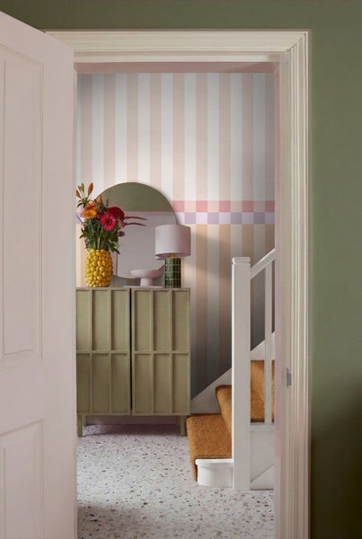 Flur mit gestreifter Tapete, Kommode, Spiegel und Treppe.