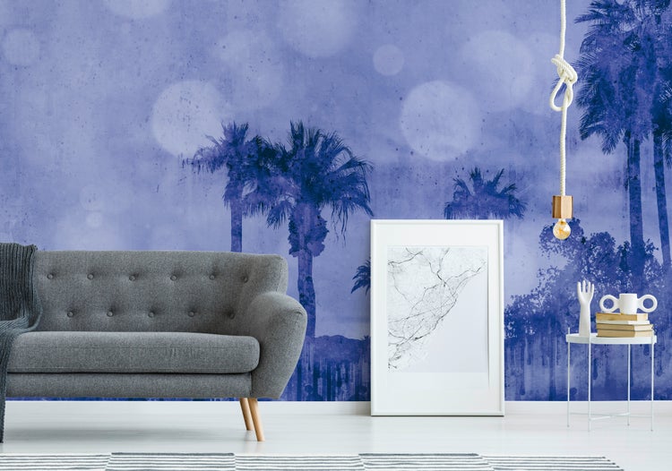 Fototapete mit Palmen-Motiv im Wohnzimmer hinter einem grauen Sofa, einem weißen Bilderrahmen und einem Beistelltisch.
