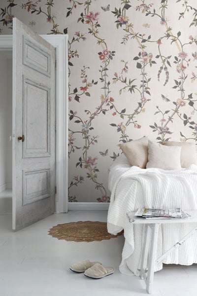 Helles Schlafzimmer mit floraler Tapete, geöffneter Holztür und weißer Bettwäsche