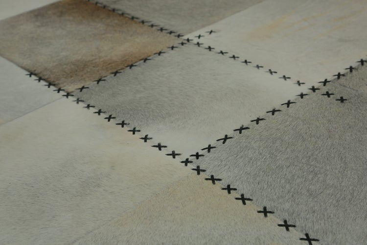 Detailaufnahme eines Patchwork-Teppichs aus Kuhfell mit sichtbaren Kreuzstich-Nähten zwischen den quadratischen Lederstücken.