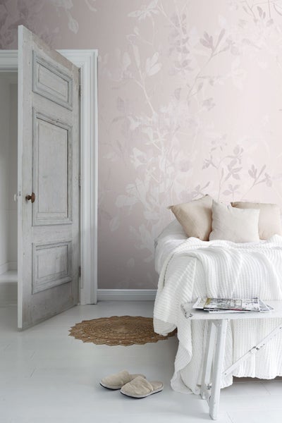 Helles Schlafzimmer mit floraler Tapete, Bett, Tisch und geöffneter Tür