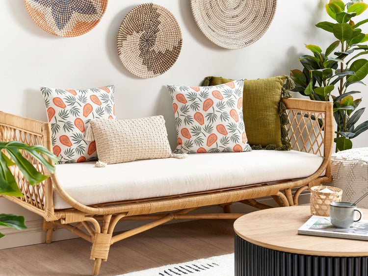 Szene mit einem Rattansofa, Dekokissen, einem runden Tisch und Zimmerpflanzen für eine gemütliche Raumatmosphäre.