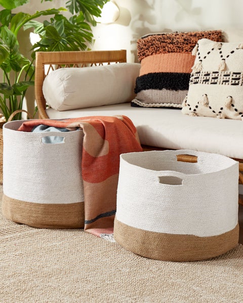 Szene mit zwei geflochtenen Körben auf einem Teppich mit Kissen und einer Decke auf einer Bank