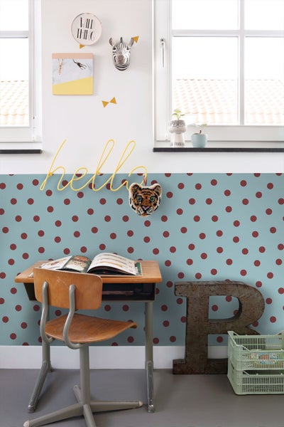 Hellblau gepunktete Tapete in einem hellen Kinderzimmer mit Holzschreibtisch, Stuhl und verschiedenen Wanddekorationen.