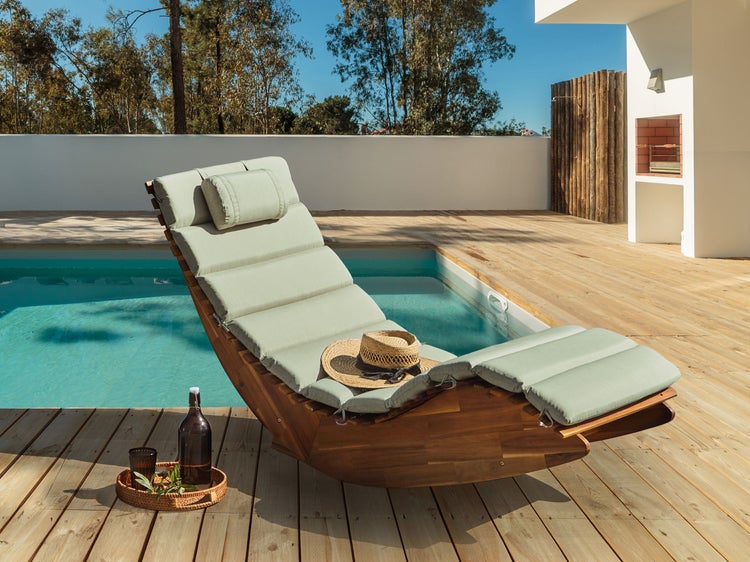 Szene mit Holzliege mit Auflage und Accessoires am Pool