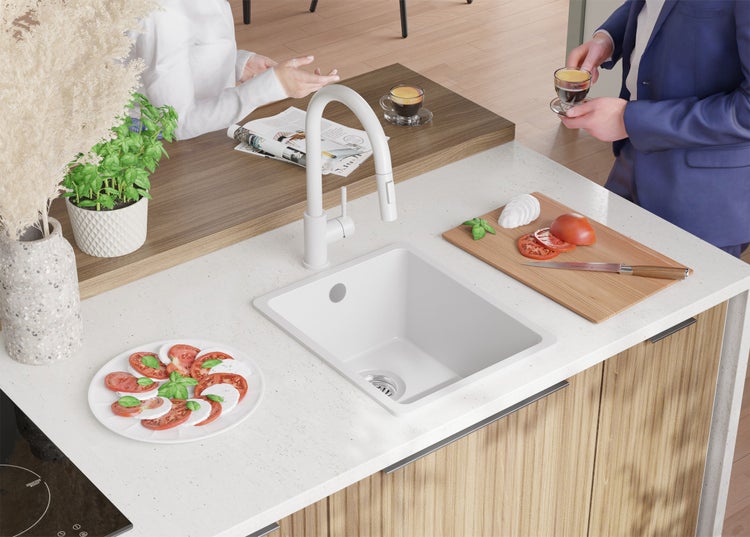 Küchenszene mit Spüle, Armatur, Schneidebrett, Mozzarella-Tomaten-Salat und zwei Personen