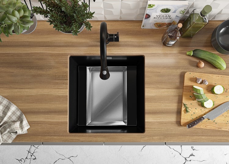 Ansicht von oben auf eine Küchenspüle mit Abtropfschale, Armatur, Spülbecken, Schneidebrett mit Zucchini und Kräutern