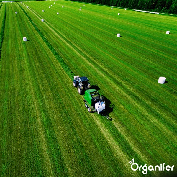 Ansicht von oben eines Traktors mit Ballenpresse auf einem Feld mit Heuballen.